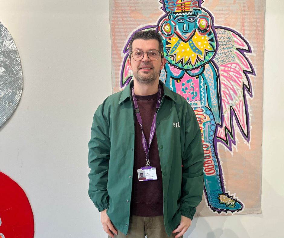 Artist Keith Clapson dressed in a green jacket standing in front of a colorful art work